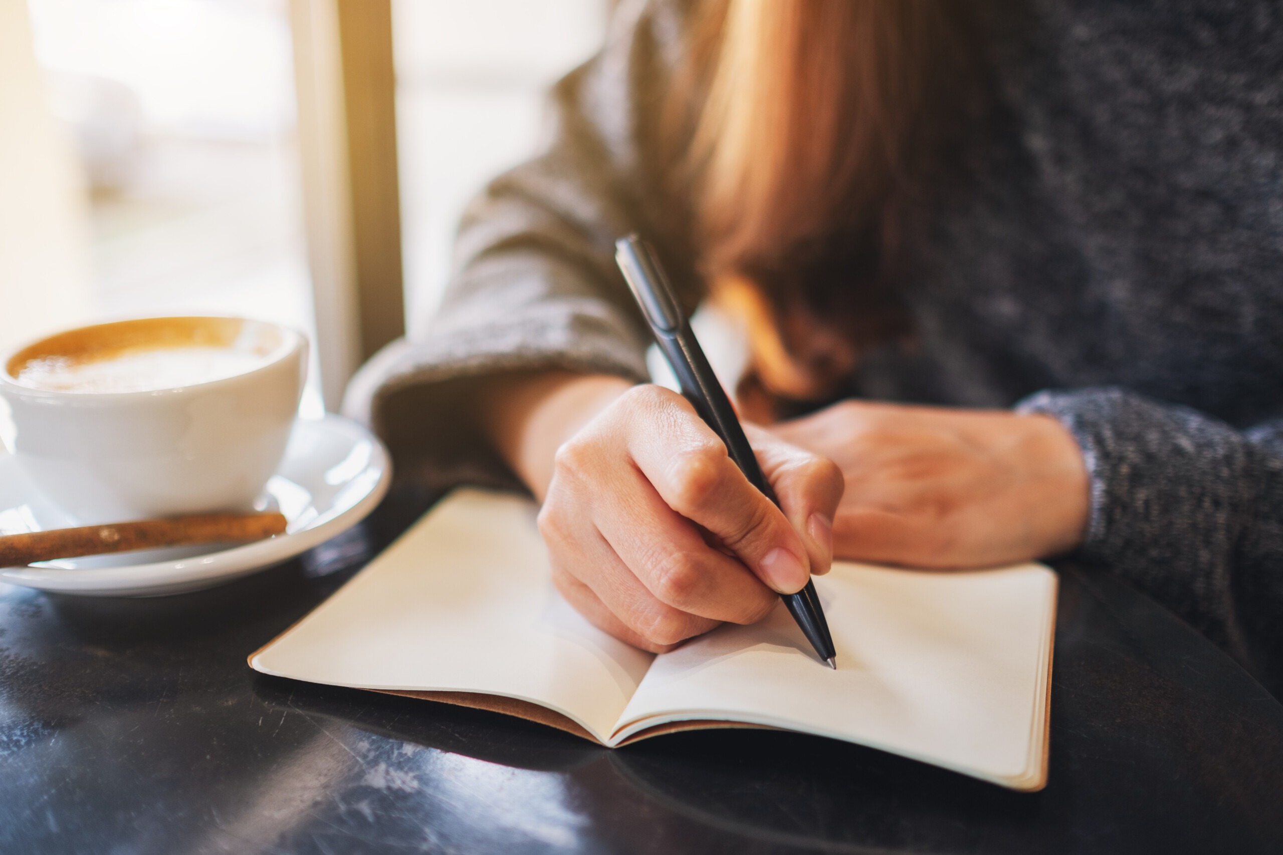 Closeup image of a woman writing on a blank notebook on the tabl